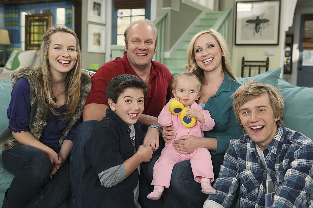 Bridgit Mendler, Jason Dolley, Bradley Steven Perry, Mia Talerico, Leigh-Allyn Baker, and Eric Allan Kramer smile together on a living room set