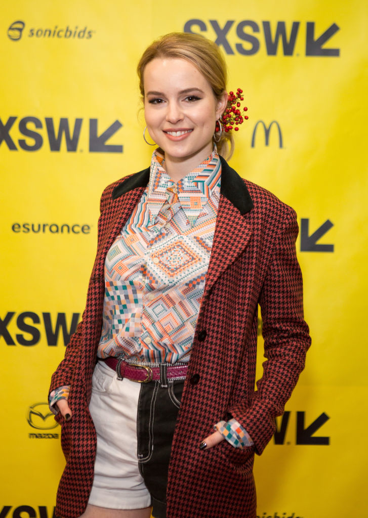 Bridgit Mendler on the SXSW red carpet, wearing a houndstooth coat over a geometric patterned shirt, white shorts with a black side panel, and a pink belt
