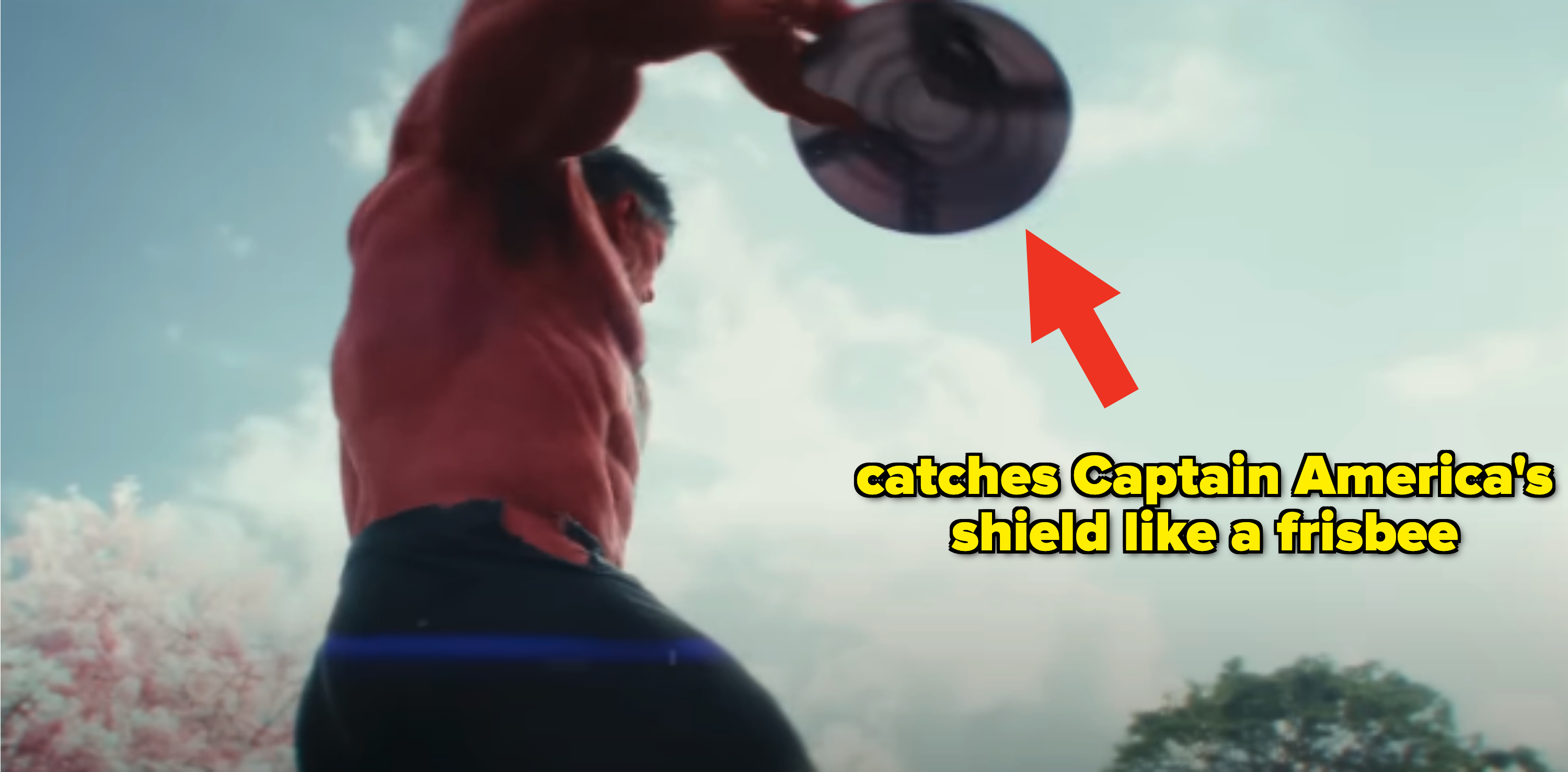 A muscular man is shown from a low angle, lifting a circular object above his head outdoors, with trees and the sky in the background