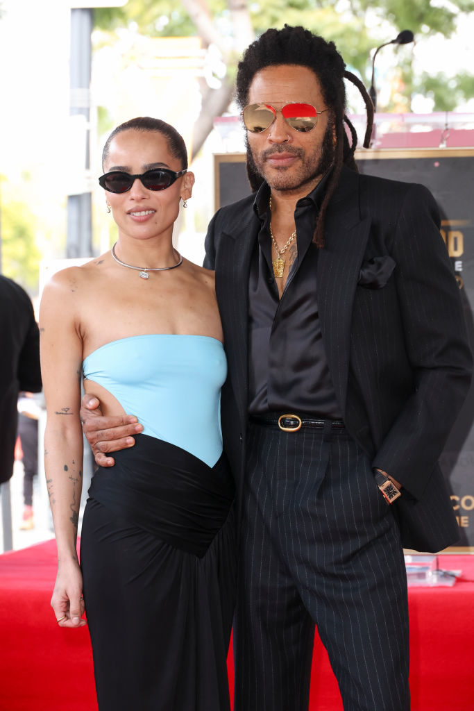 Zoe Kravitz and Lenny Kravitz pose together; Lenny wears a black suit with pinstripe pants and aviator sunglasses, and Lisa wears an off-shoulder dress with sunglasses