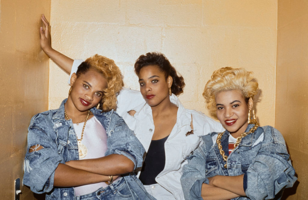 Salt-N-Pepa pose together in trendy 1980s denim outfits, each sporting gold jewelry and vibrant hairstyles