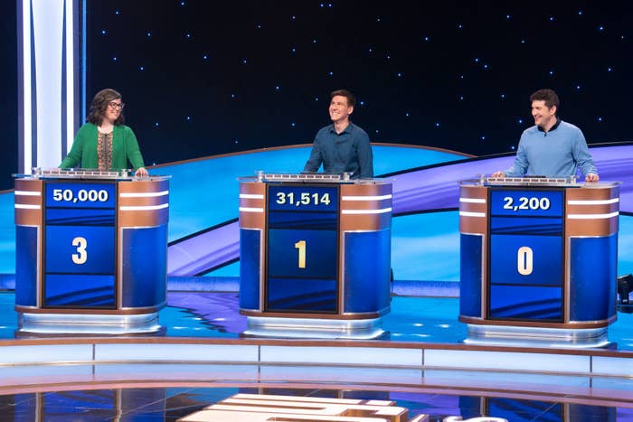 Three contestants standing at podiums displaying scores: 50,000; 31,514; and 2,200, during a game show