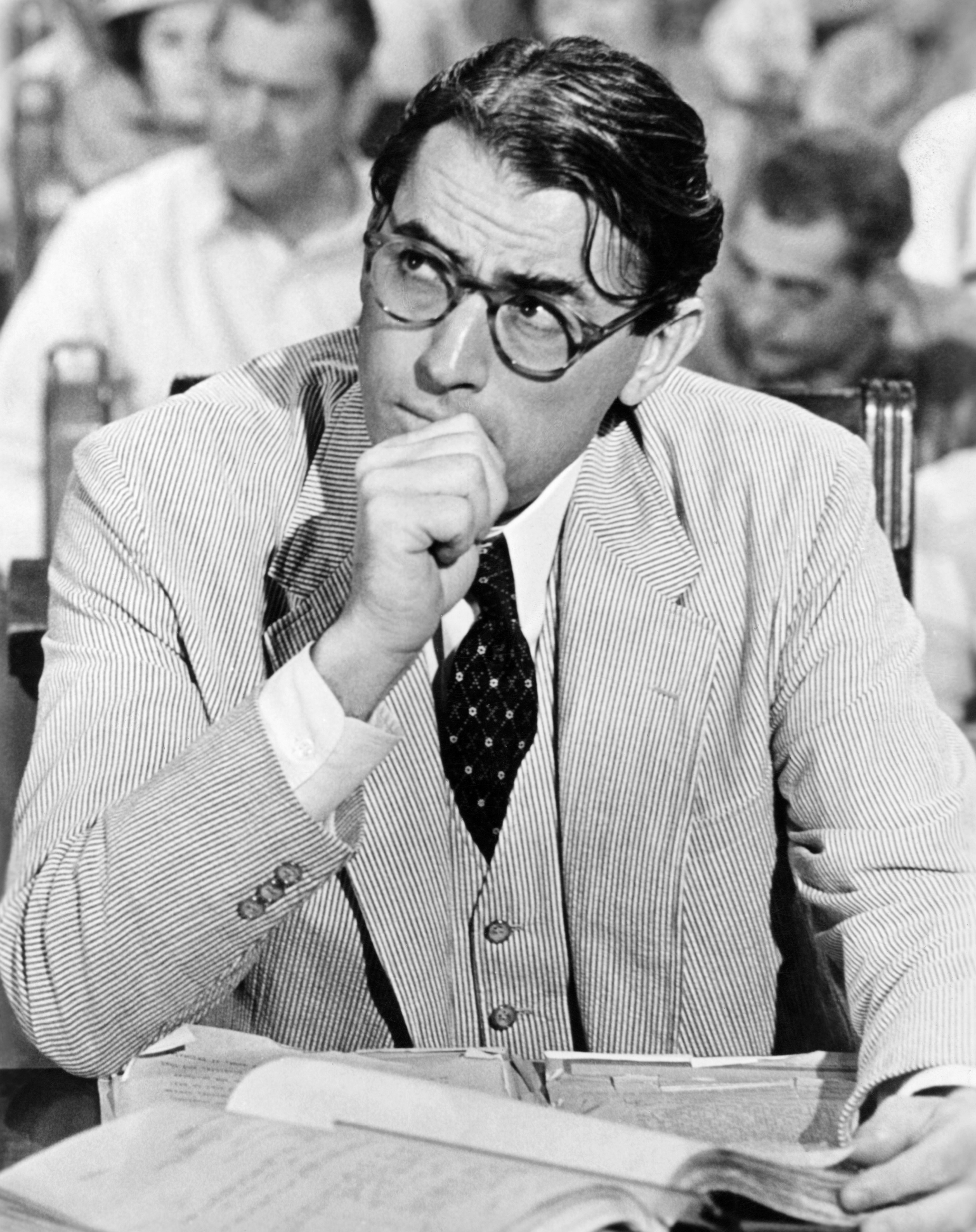 I don't know who they are. The person is sitting at a desk wearing a pinstriped suit, a patterned tie, and glasses, appearing to be in deep thought