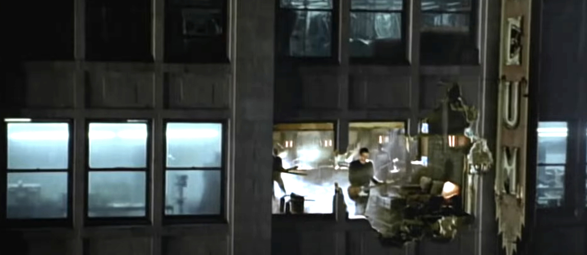 A person dangles off a high-rise building sign while another person inside the building tries to help them