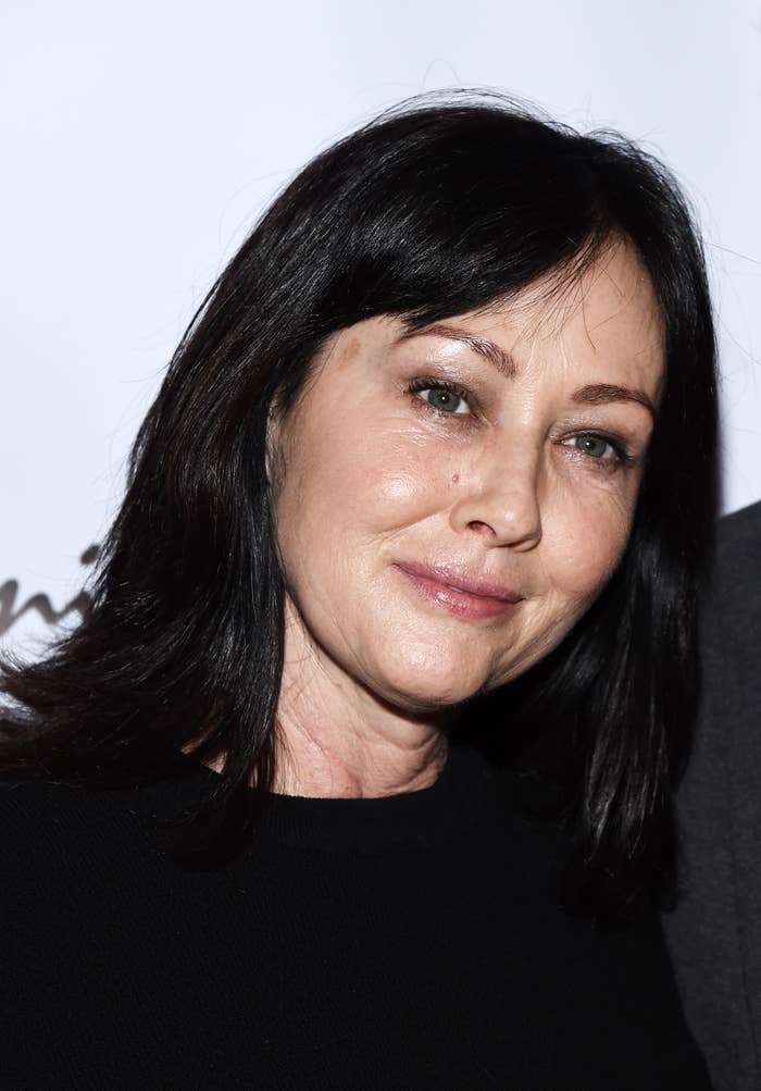Shannen Doherty smiles softly at an event, wearing a simple black top