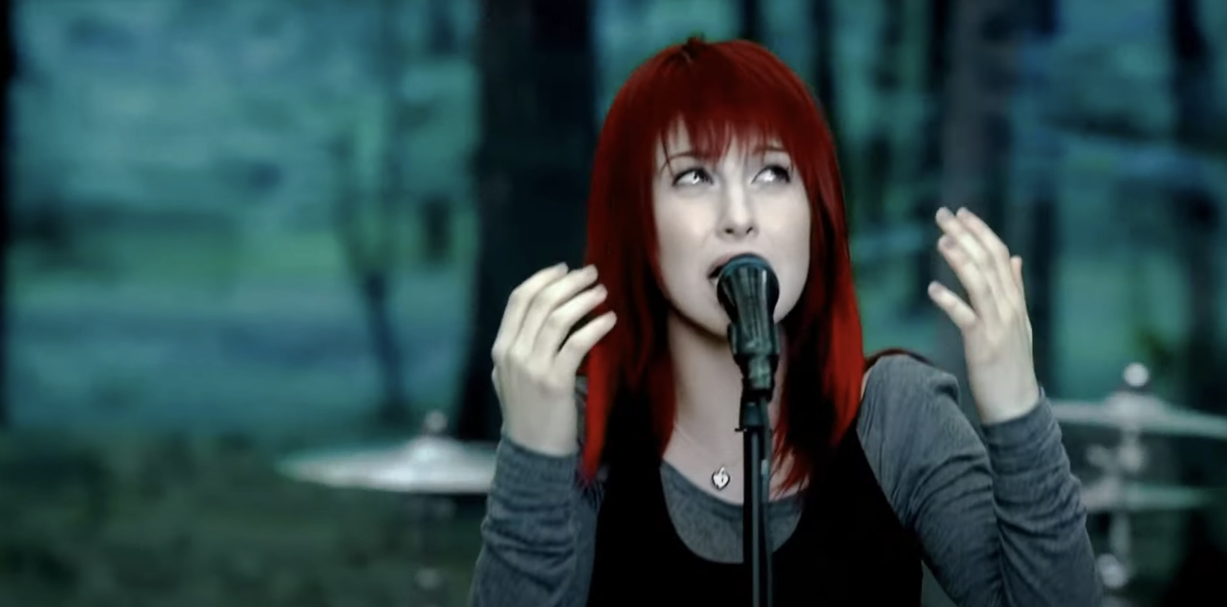Hayley Williams sings into a microphone with hands raised, set against a blurred background