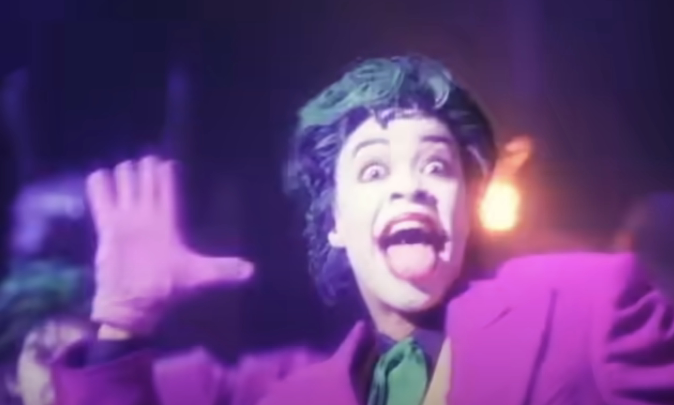 Person dressed as the Joker character, wearing a suit with theatrical makeup and exaggerated facial expression