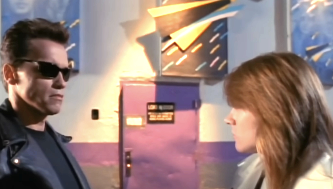 Arnold Schwarzenegger in a black leather jacket and sunglasses faces faces a band member of Guns 'N Roses