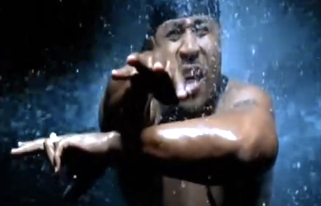 LL Cool J performs energetically, gesturing with his hands amidst a spray of water in a music video scene