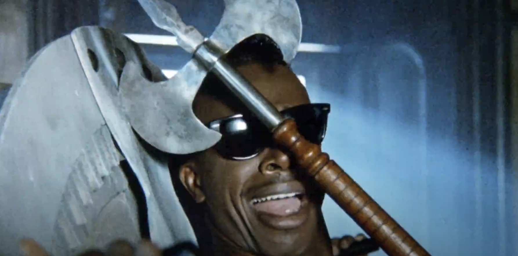 Man wearing sunglasses, screaming with a large axe embedded in his head