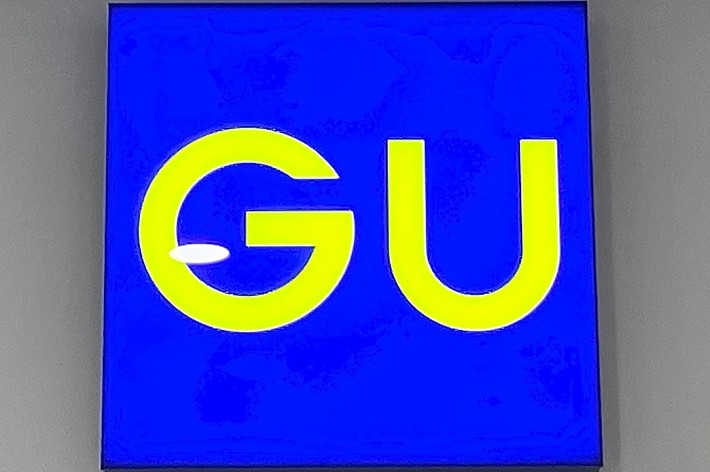 A sign with the letters “GU” in bright yellow, displayed on a solid background