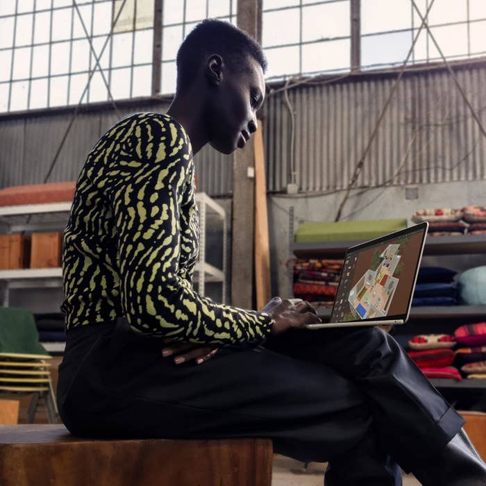 Person in a patterned top and dark pants uses a laptop in a modern, industrial-styled interior