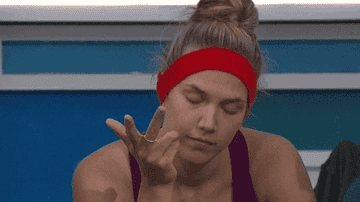 A woman with a red headband and a purple sleeveless top rolls her eyes and waves her hand dismissively