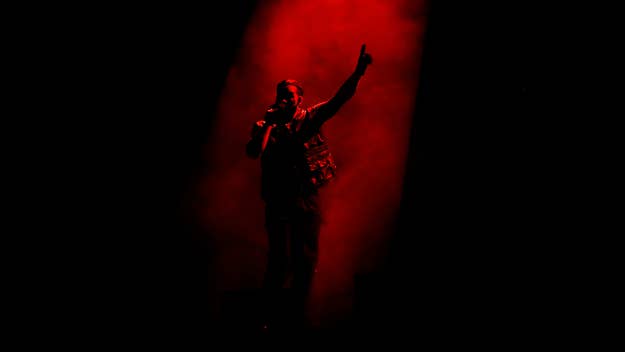 A person on stage points upwards while holding a microphone, partially obscured by red smoke, creating a dramatic effect