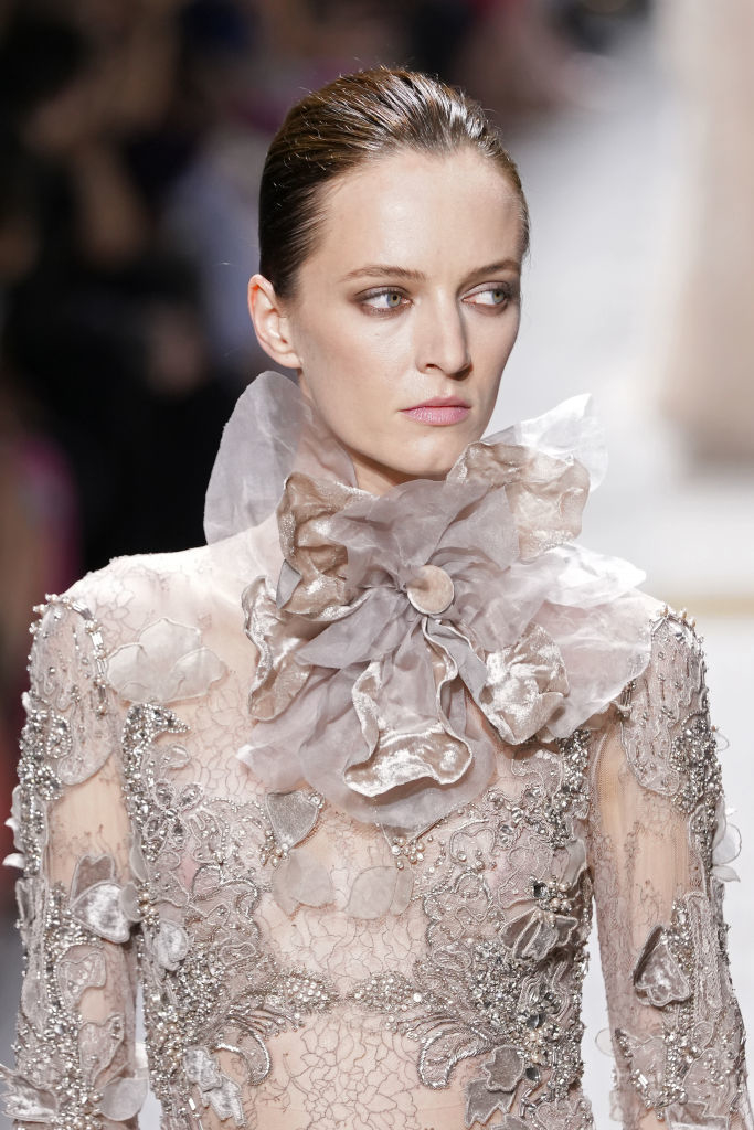 Daria Strokous wearing a high-collared, intricately embellished dress with floral details, walking on a fashion runway