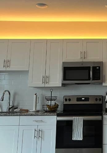 Modern kitchen with white cabinets, stainless steel appliances, and a striped towel hanging from the oven door