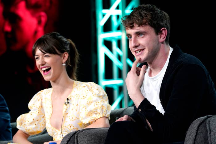 Daisy Edgar-Jones in a puff-sleeve dress with yellow patterns sits laughing next to Paul Mescal, who is smiling and wearing a dark jacket and white shirt