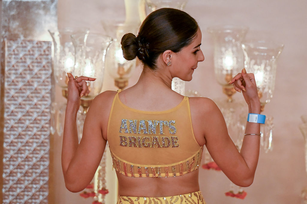 Ananya Panday, in a glamorous dress, poses pointing to the "Anant's Brigade" text on her outfit at a celebrity event