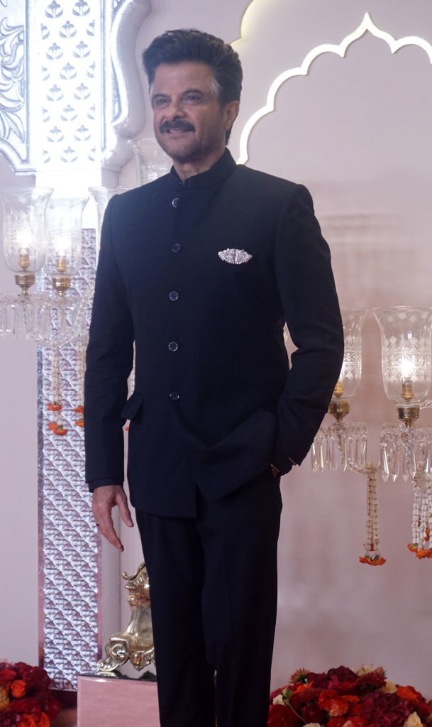 Anil Kapoor poses in a stylish, tailored suit at a formal event with ornate decorations in the background