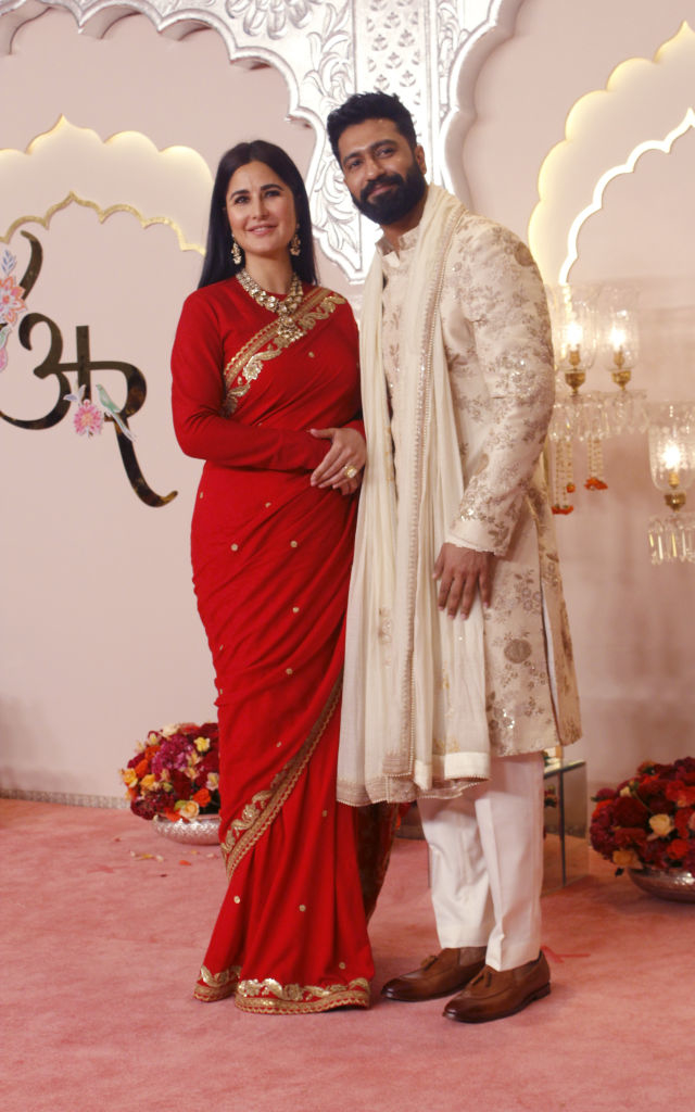 Katrina Kaif in a sari and Vicky Kaushal in a traditional outfit pose together on a red carpet, standing in front of a floral backdrop