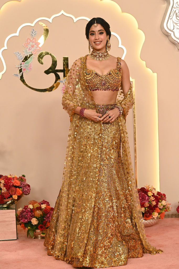 Janhvi Kapoor on a red carpet, wearing an ornate lehenga with a heavily embroidered blouse and matching dupatta