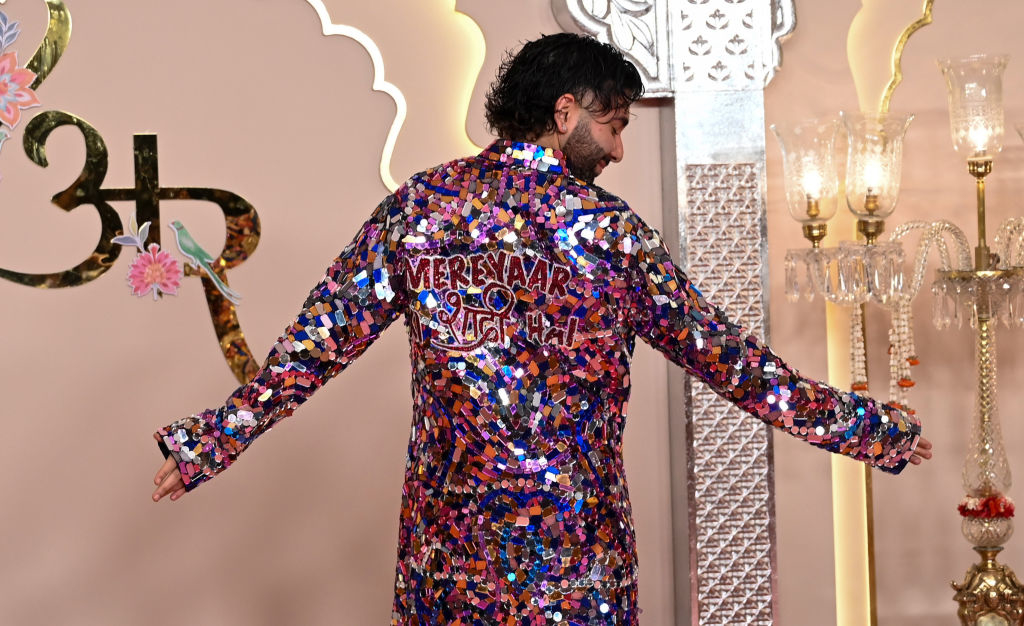 Orry wearing a long, colorful sequined coat with writing on back