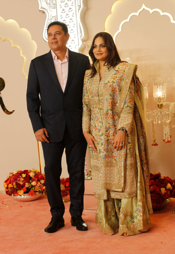 Atul in a dark suit and Alvira in an embroidered traditional outfit stand together, posing for a photo in a decorated venue