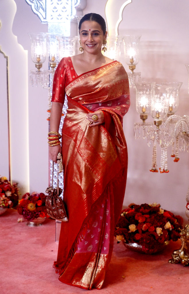 Vidya Balan wearing a traditional sari at a formal event, carrying a small clutch and adorned with jewelry