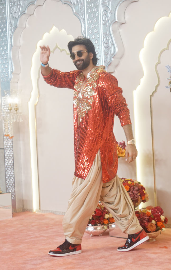 Meezaan Jafri waves, wearing a traditional outfit with a sequined top and neutral pants, along with sneakers, at an event