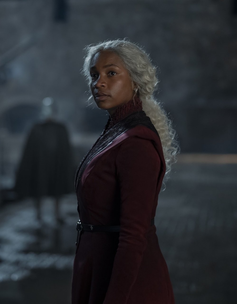 Mujer con vestido de estilo medieval, parado en un entorno oscuro y antiguo con cabello largo y rizado