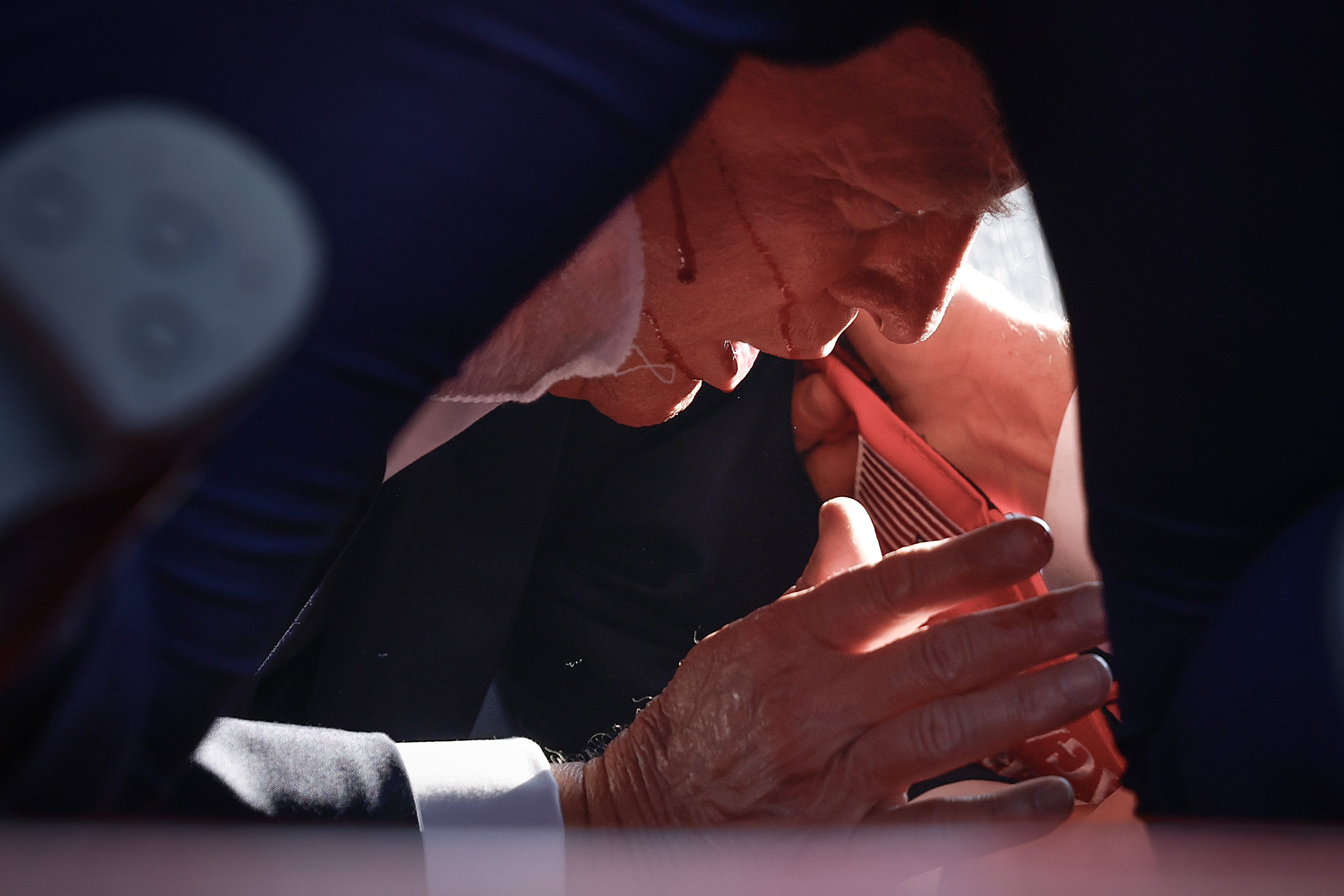U.S. former president Donald Trump leans into a fall on stage with his hands outstretched, prompting concern and assistance from nearby individuals