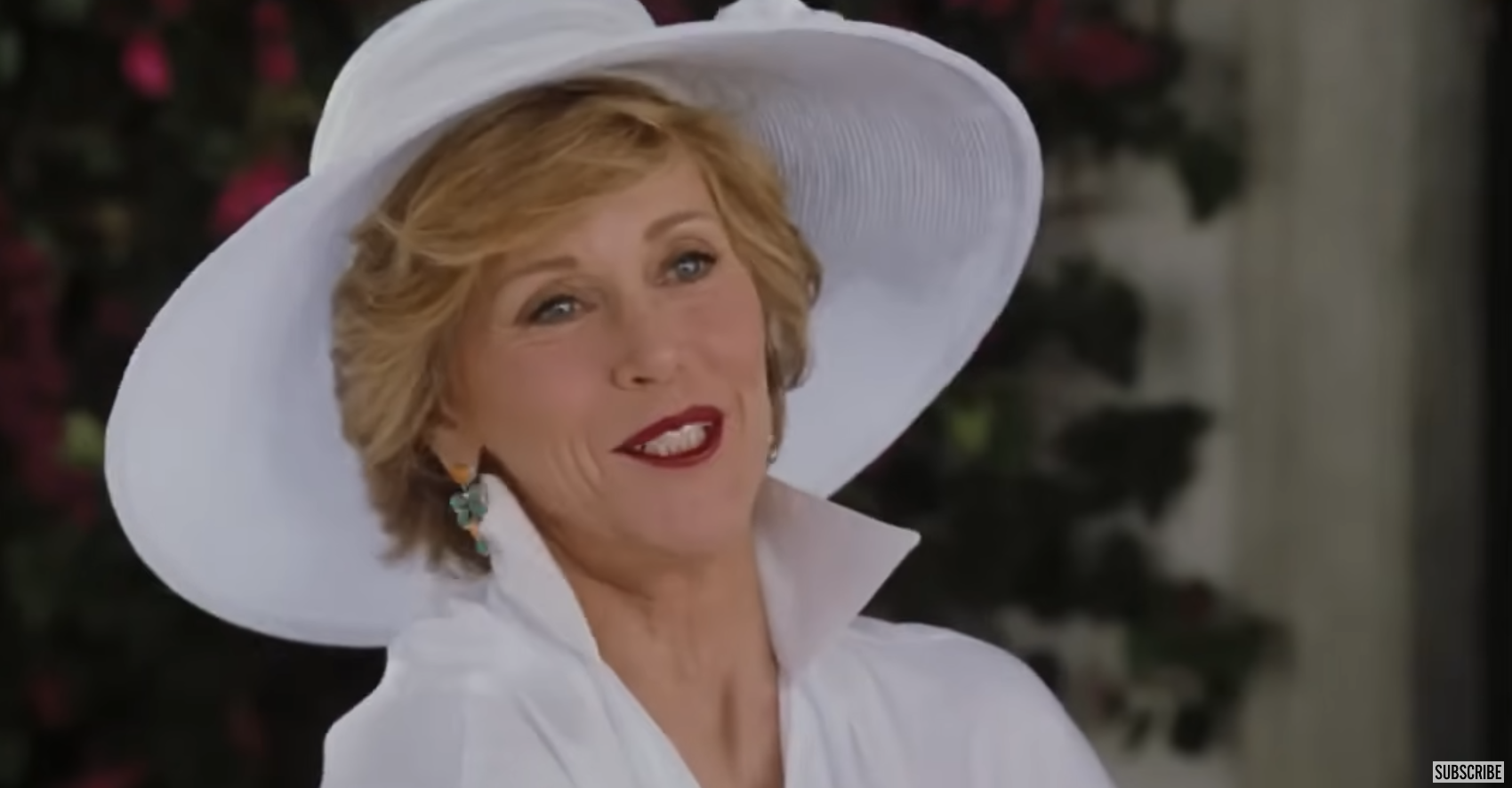 Jane Fonda wearing a wide-brimmed hat, white outfit, and teal earrings, smiling warmly