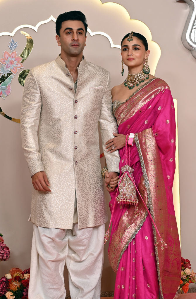 Ranbir Kapoor and Alia Bhatt hold hands at an event. Ranbir is in a traditional sherwani, while Alia wears an ornate saree with heavy jewelry