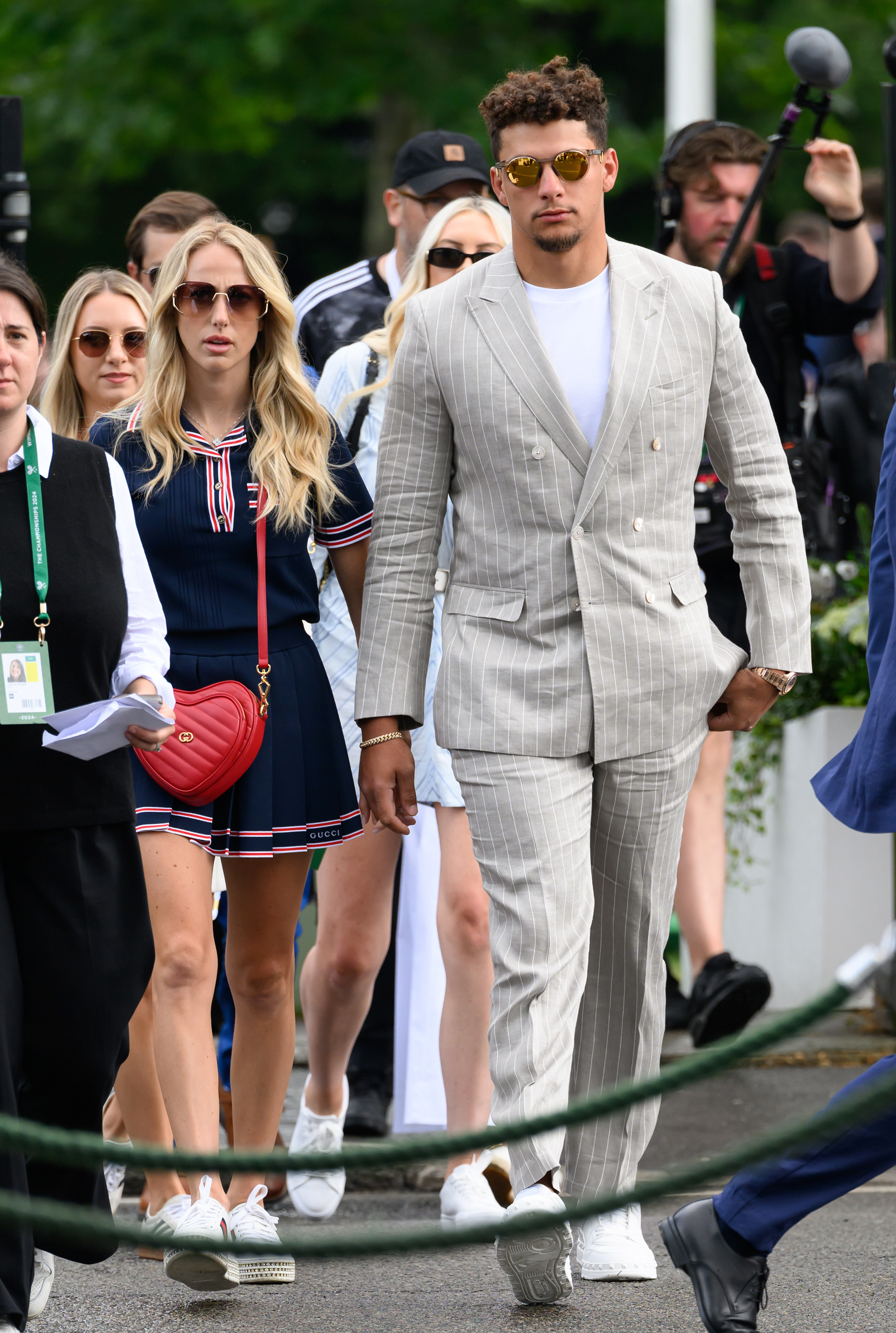 Patrick Mahomes in a light pinstriped suit and Brittany Mahomes in a sporty dress walking outdoors accompanied by others