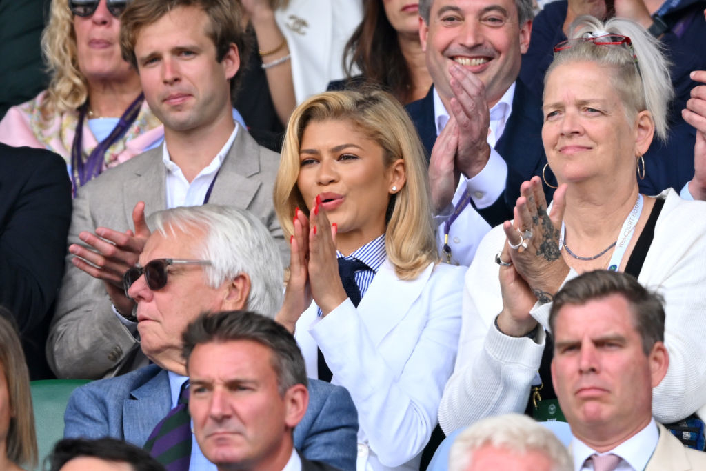 Zendaya in the stands clapping at an event, surrounded by a group of spectators