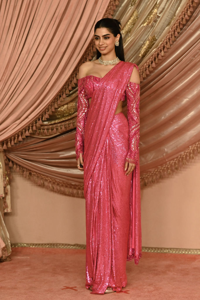 Actor Khushi Kapoorat an event, wearing an off-shoulder, sequined sari with matching long gloves and a diamond necklace. She stands in front of ornate drapery
