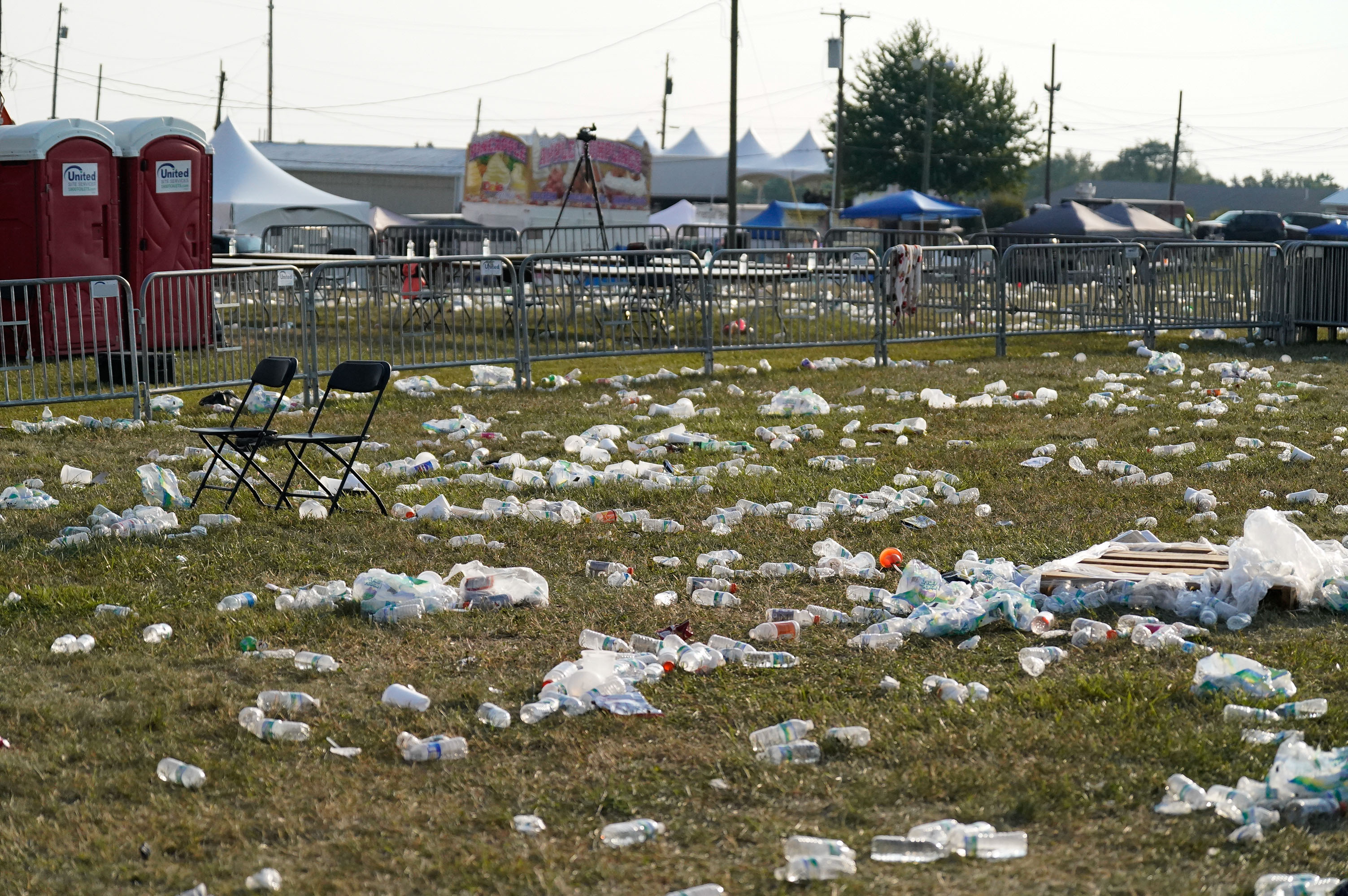 Empty event grounds littered with plastic bottles and trash, with two empty folding chairs near portable toilets