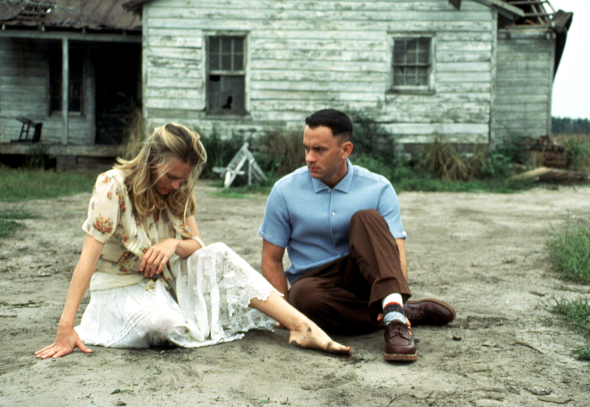 Robin Wright and Tom Hanks as Jenny and Forrest Gump sitting on the ground outside a weathered wooden house in a scene from the movie "Forrest Gump."