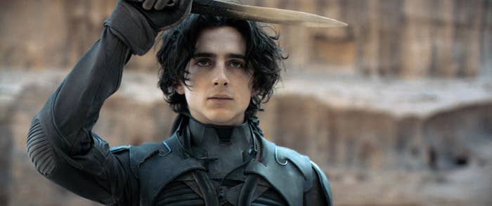Timothée Chalamet in a still from the movie "Dune," holding a knife while wearing futuristic armor