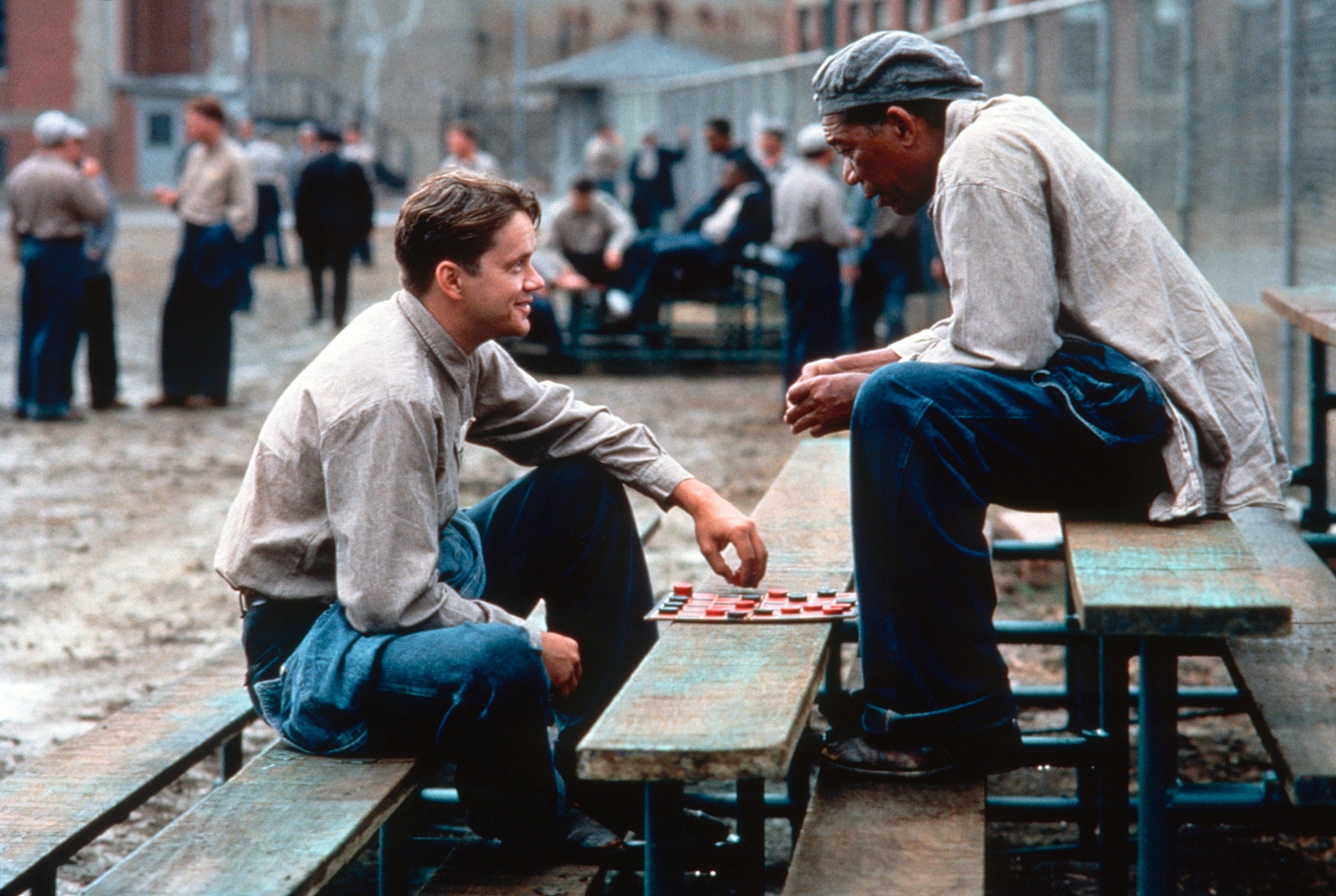 Tim Robbins and Morgan Freeman in a scene from The Shawshank Redemption, playing checkers on a bench in the prison yard with other inmates in the background