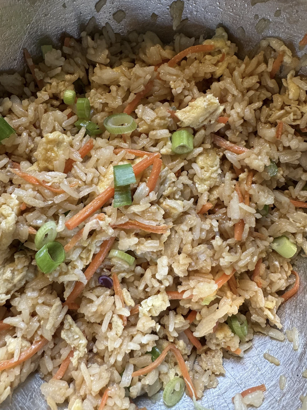 A close-up image of fried rice with sliced green onions, shredded carrots, and scrambled eggs