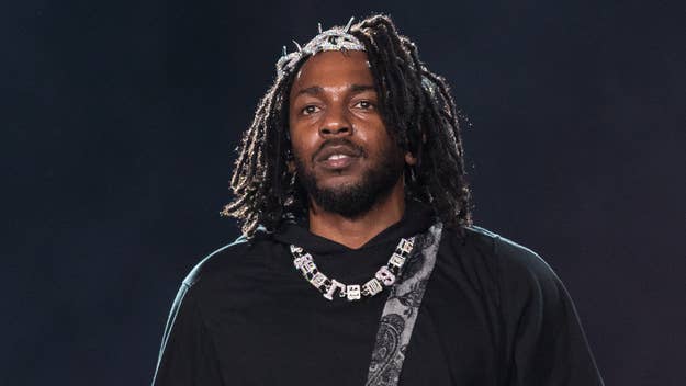 A man with dreadlocks, wearing a decorative necklace and a black top, stands on stage