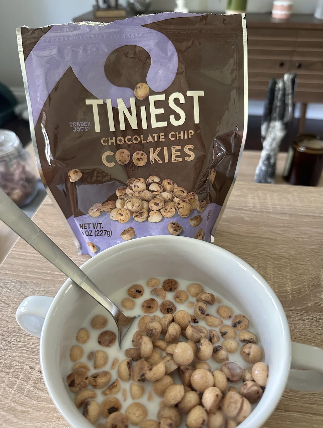 A bowl of milk with tiny chocolate chip cookies, with a bag of Trader Joe's &quot;Tiniest Chocolate Chip Cookies&quot; in the background showing the product
