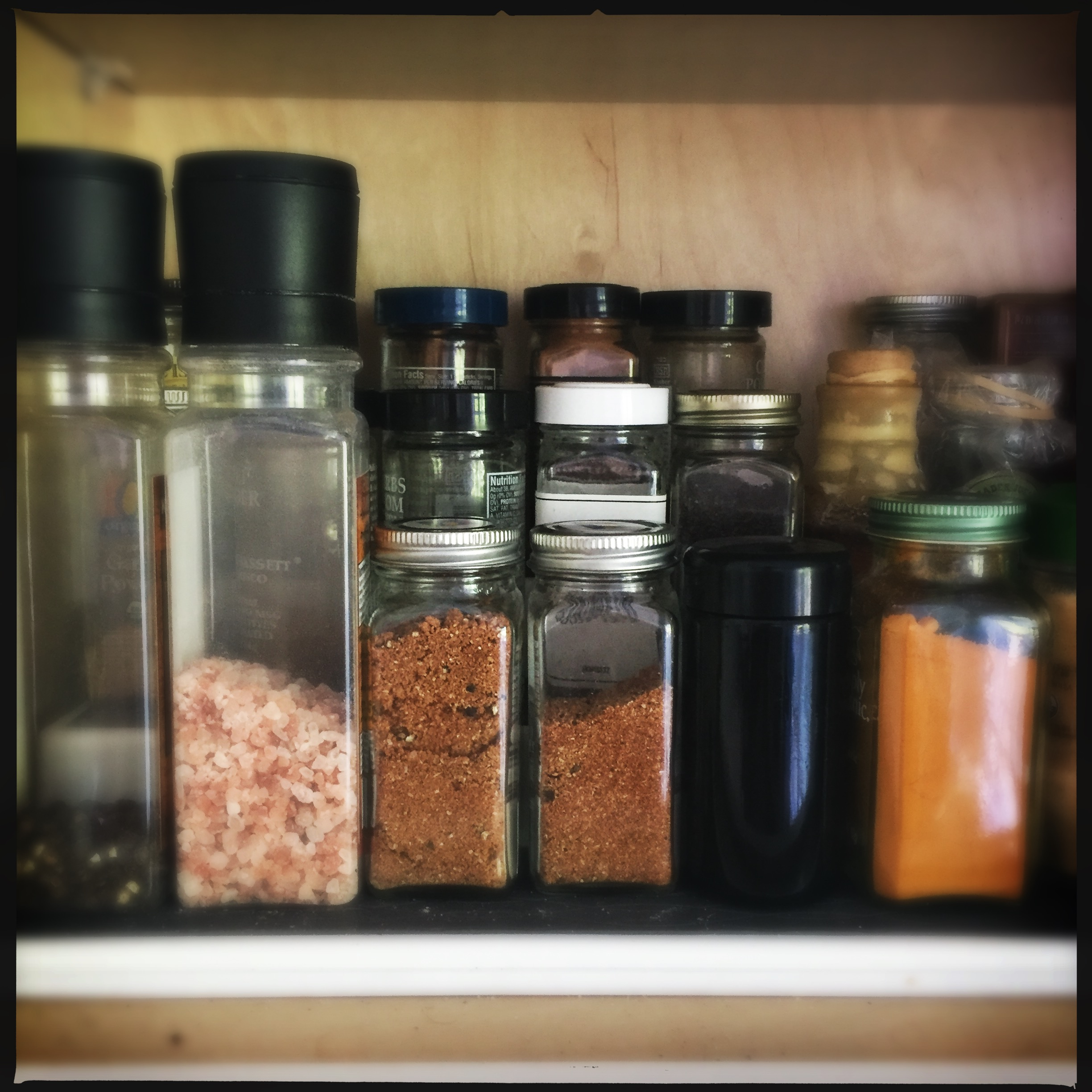 Various spice jars and containers arranged on a wooden shelf in a kitchen cabinet