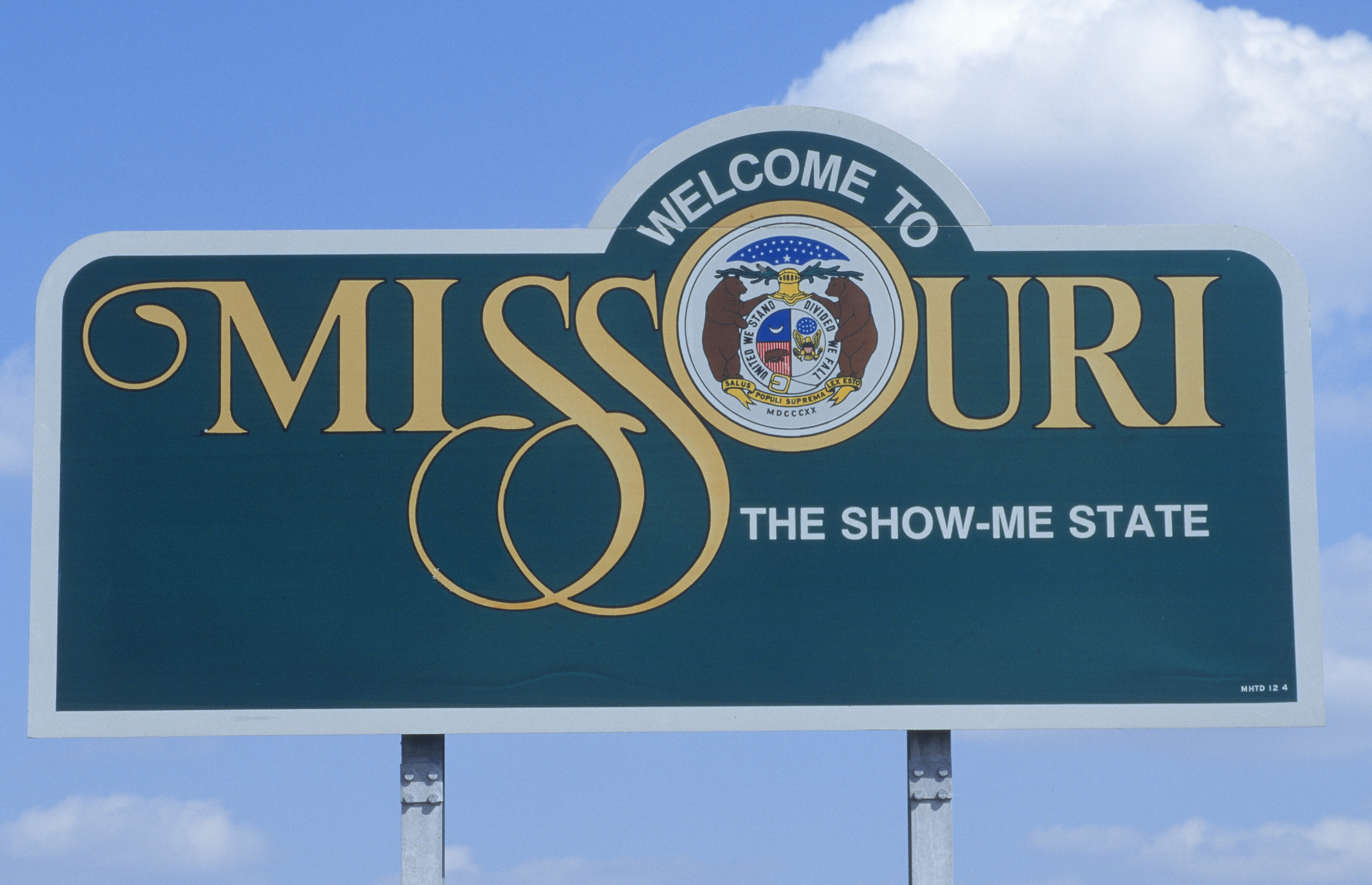 Welcome to Missouri sign with the state seal and "The Show-Me State" motto against a blue sky