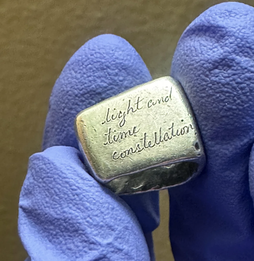 A person wearing blue gloves holds a small silver object engraved with the words "light and time constellation."
