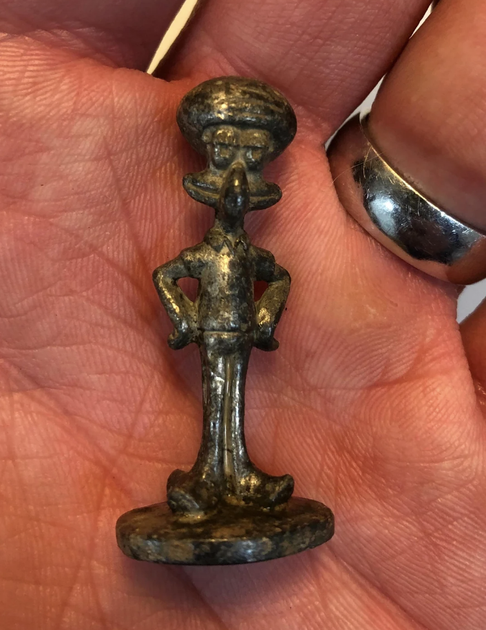 A hand holds a small vintage figurine of the animated character Squidward Tentacles from SpongeBob SquarePants