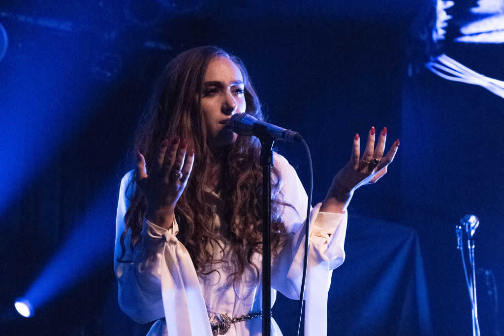 Chappell Roan wearing a long-sleeved blouse, performs passionately on stage, holding a microphone and gesturing with their hands