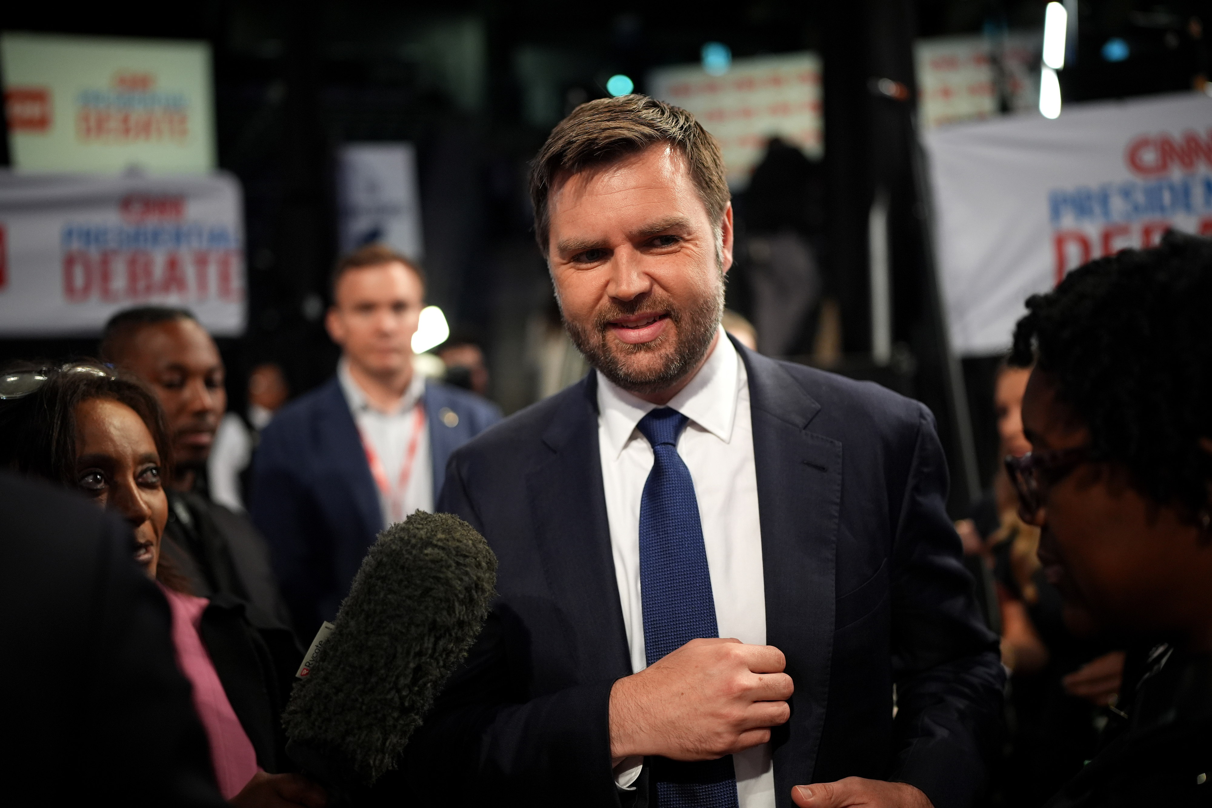 A man in a suit and tie is surrounded by microphones and reporters at a CNN presidential debate event