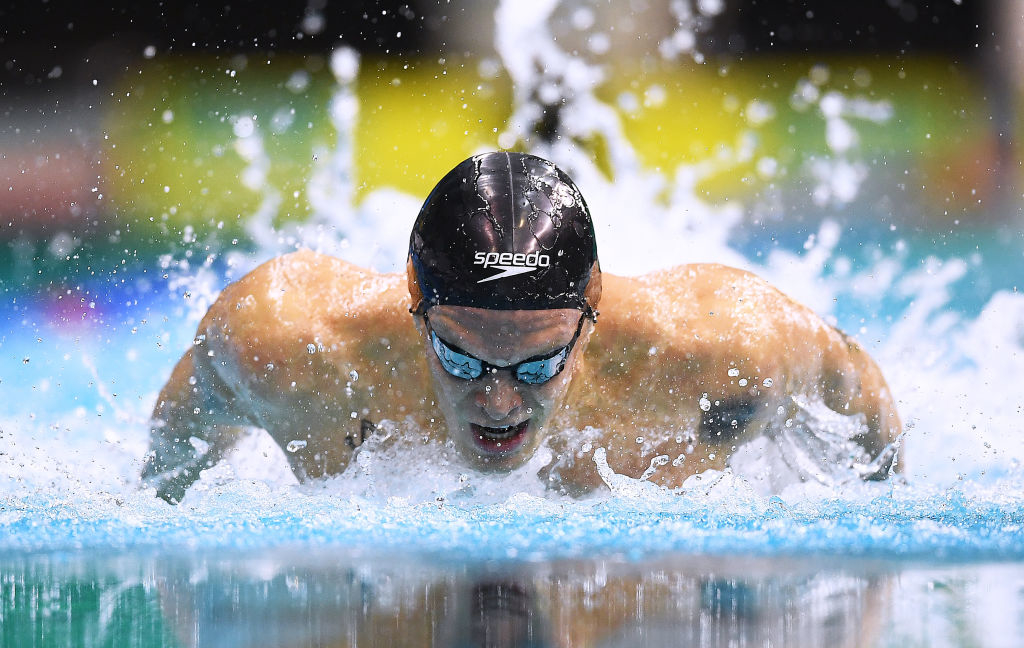 Cody Simpson in action during a butterfly stroke race, wearing a Speedo swim cap and goggles